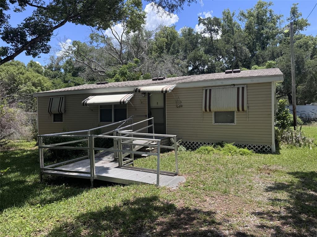 A single-story mobile home with tan siding and an aluminum wheelchair ramp leading to the entrance — 20050 RUTH STREET, BROOKSVILLE, FL