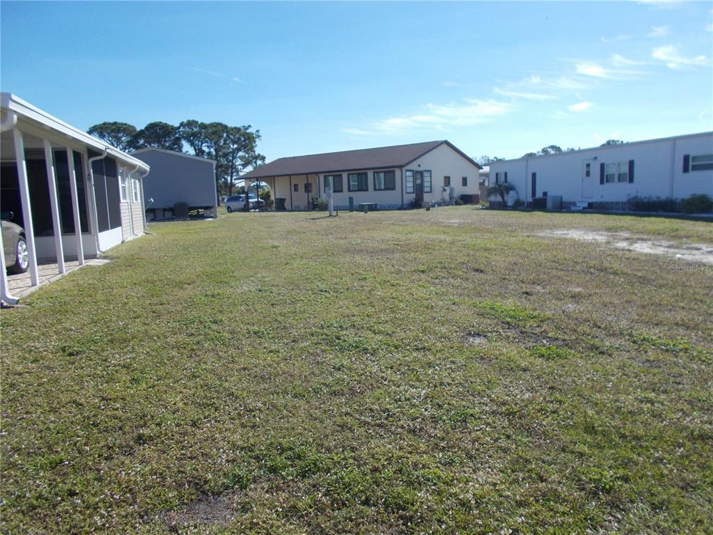 A grassy lot sits between several manufactured homes under a clear blue sky — 6824 ANAPA COURT, NORTH PORT, FL