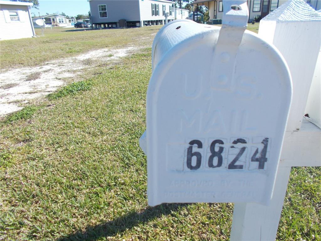 A white mailbox with the number 6824 stands in a grassy yard near mobile homes — 6824 ANAPA COURT, NORTH PORT, FL