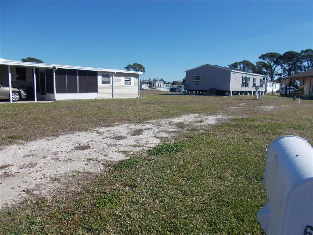 A grassy lot with a gravel driveway sits between two manufactured homes under a blue sky — 6824 ANAPA COURT, NORTH PORT, FL