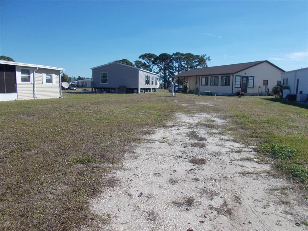 An empty dirt lot sits between several manufactured homes under a clear blue sky — 6824 ANAPA COURT, NORTH PORT, FL