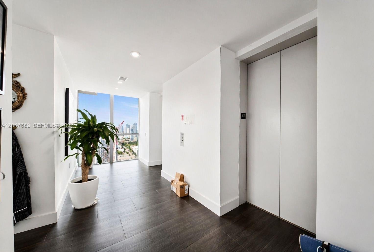A hallway features dark wood-look flooring, a potted plant, and a white elevator door — 1100 Biscayne Blvd # 3708, Miami FL 33132, MIAMI, FL