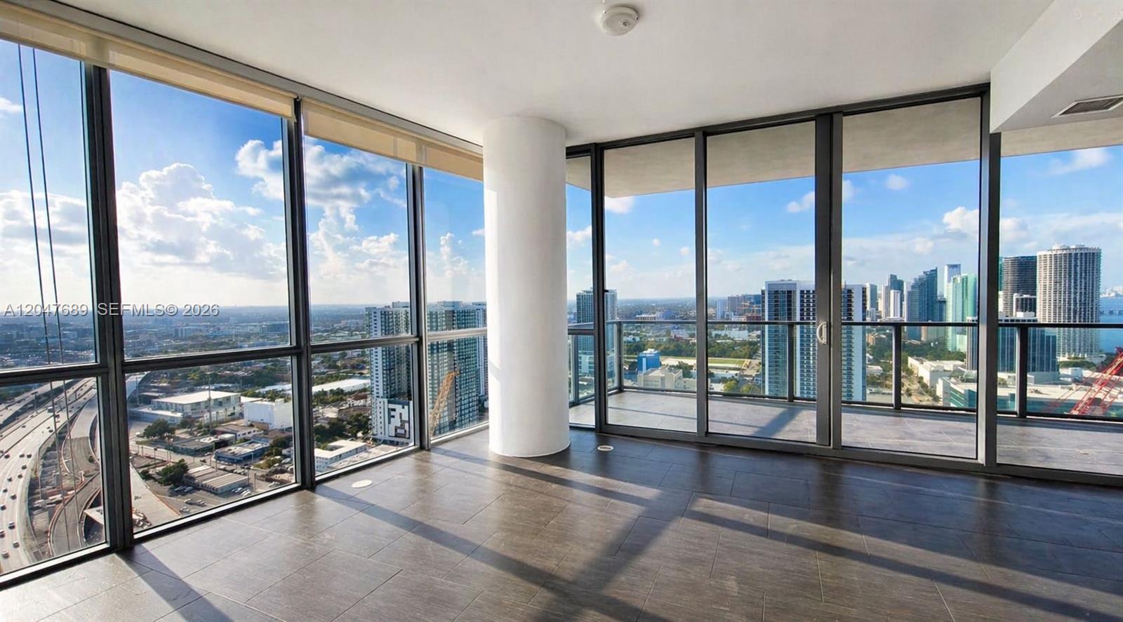 A modern room features floor-to-ceiling windows, a central white column, and dark tile flooring — 1100 Biscayne Blvd # 3708, Miami FL 33132, MIAMI, FL