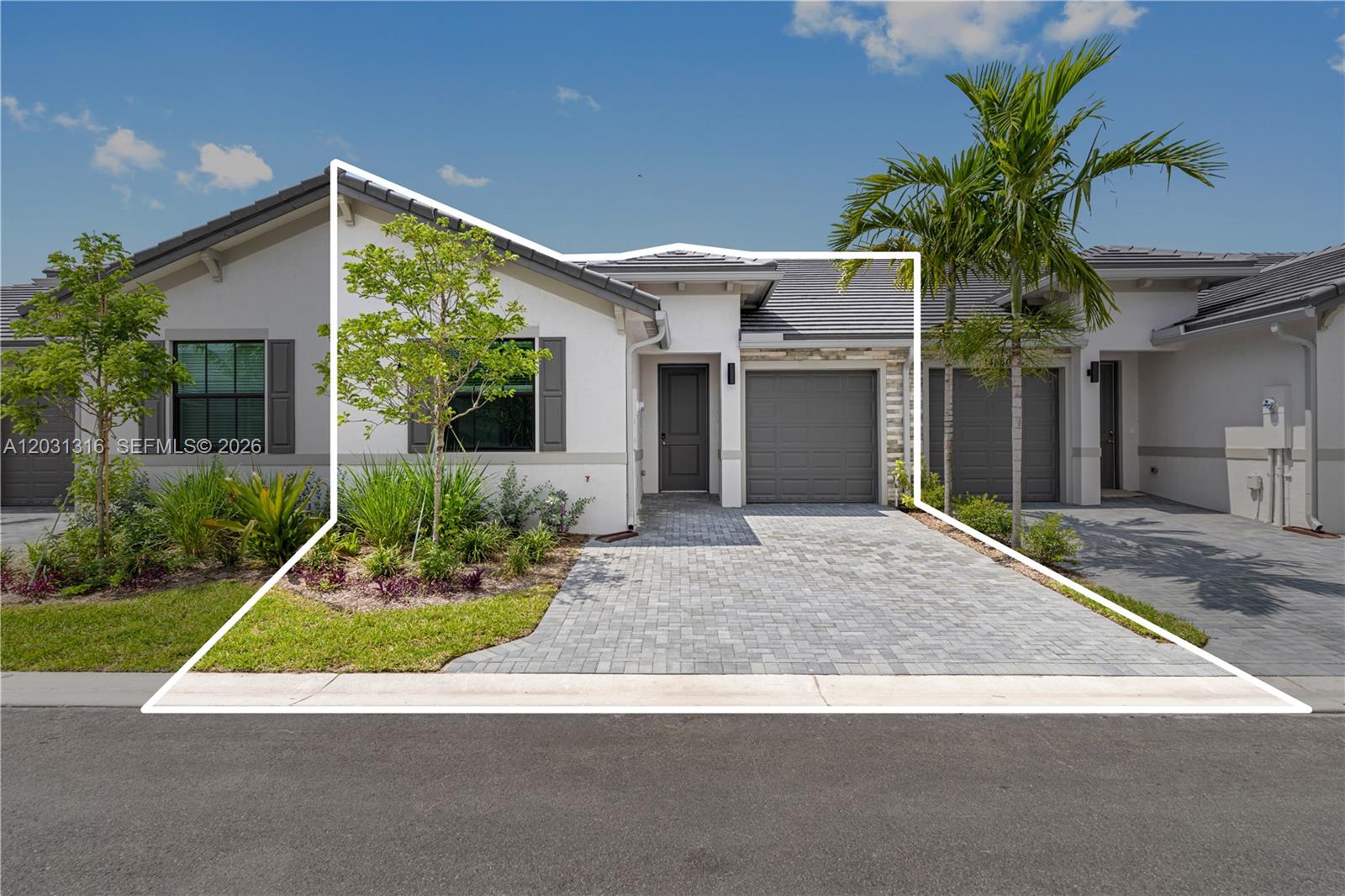 The exterior of a modern single-story townhouse features a gray garage, paved driveway, and landscaping — 7305 Ivory Spring, Delray Beach FL 33446, DELRAY BEACH, FL