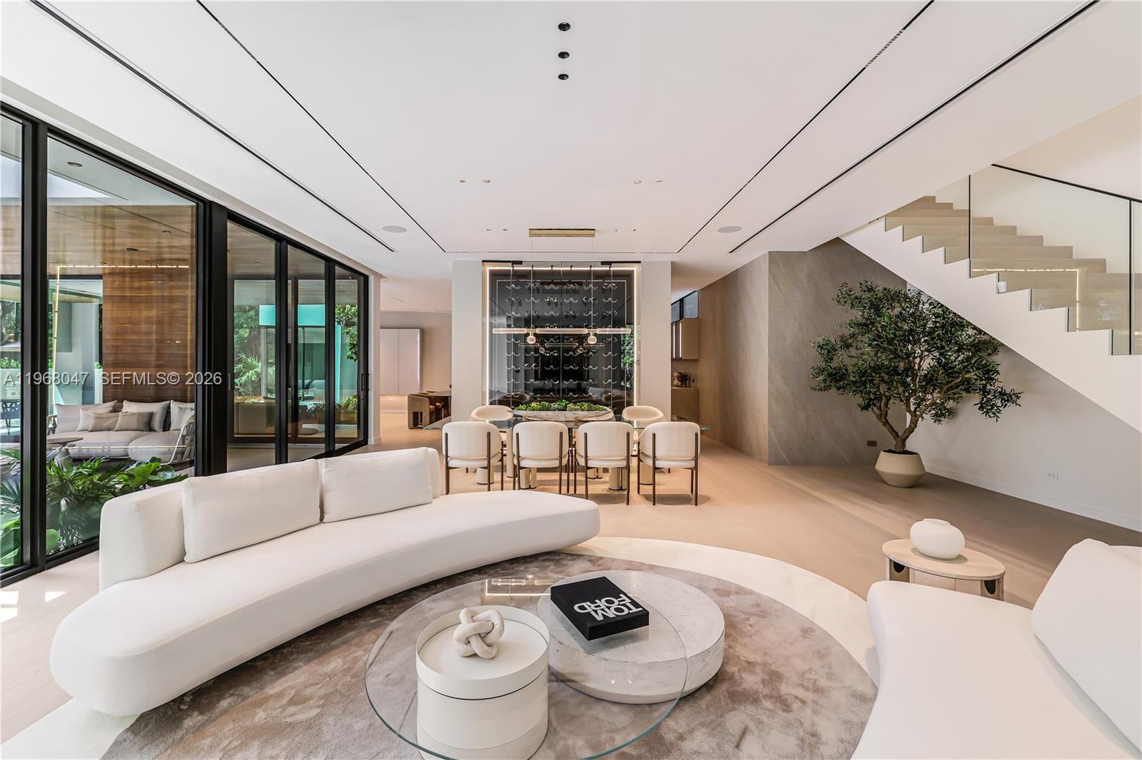 A modern open-concept living and dining area features a curved sofa, glass coffee table, and staircase — 2497 Abaco Ave, Miami FL 33133, MIAMI, FL