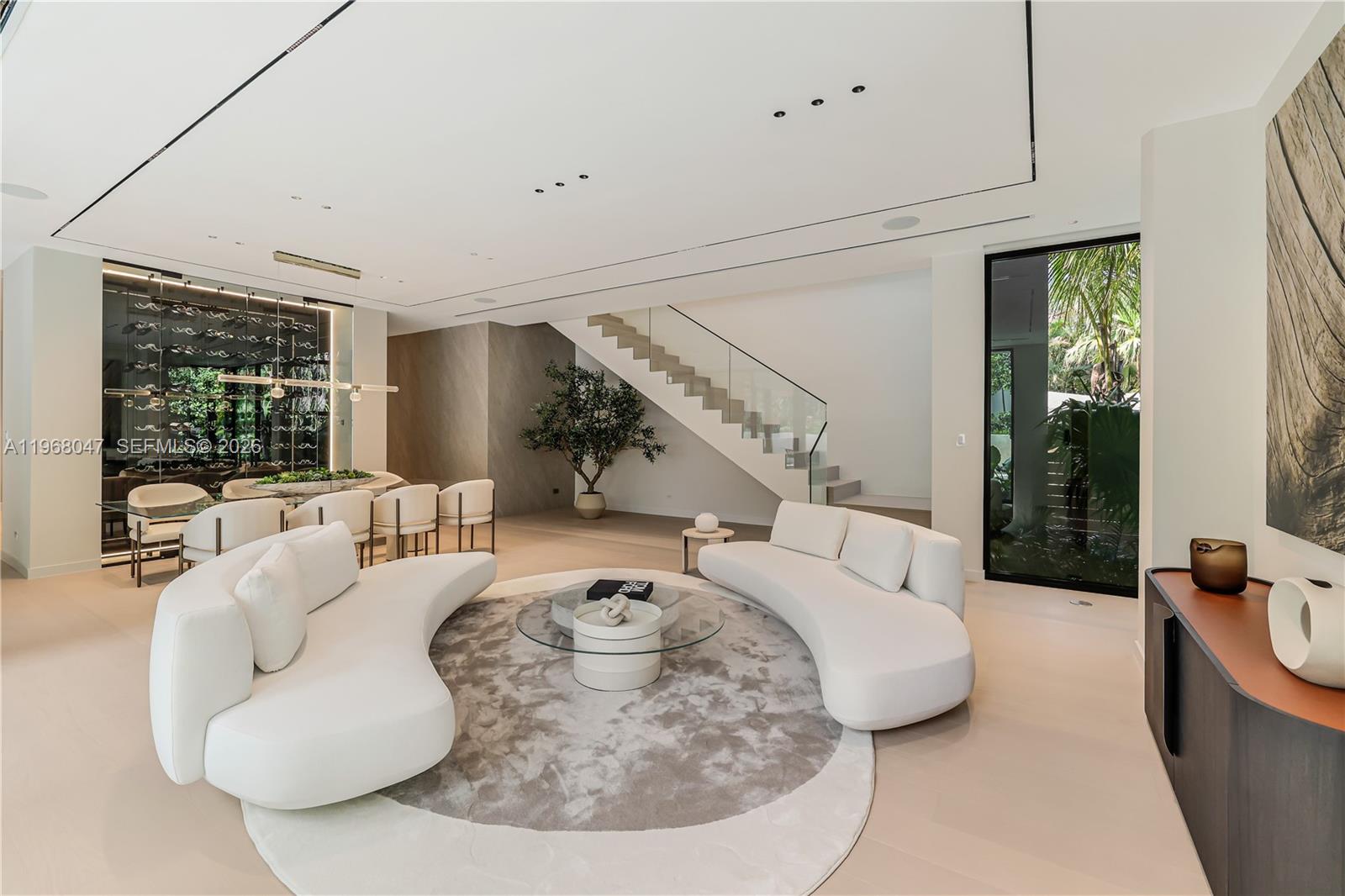 A modern living room features two curved white sofas, a circular rug, and a staircase — 2497 Abaco Ave, Miami FL 33133, MIAMI, FL