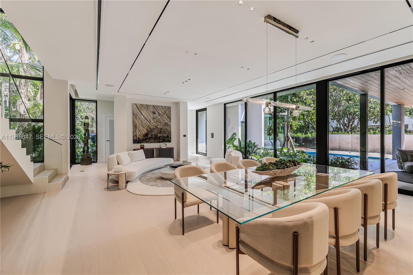 A modern open-plan living and dining area features floor-to-ceiling windows overlooking a pool — 2497 Abaco Ave, Miami FL 33133, MIAMI, FL