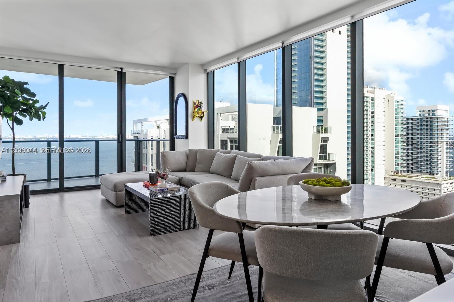 A modern living and dining area features floor-to-ceiling windows with expansive city and water views — 460 NE 28th St # 2008, Miami FL 33137, MIAMI, FL