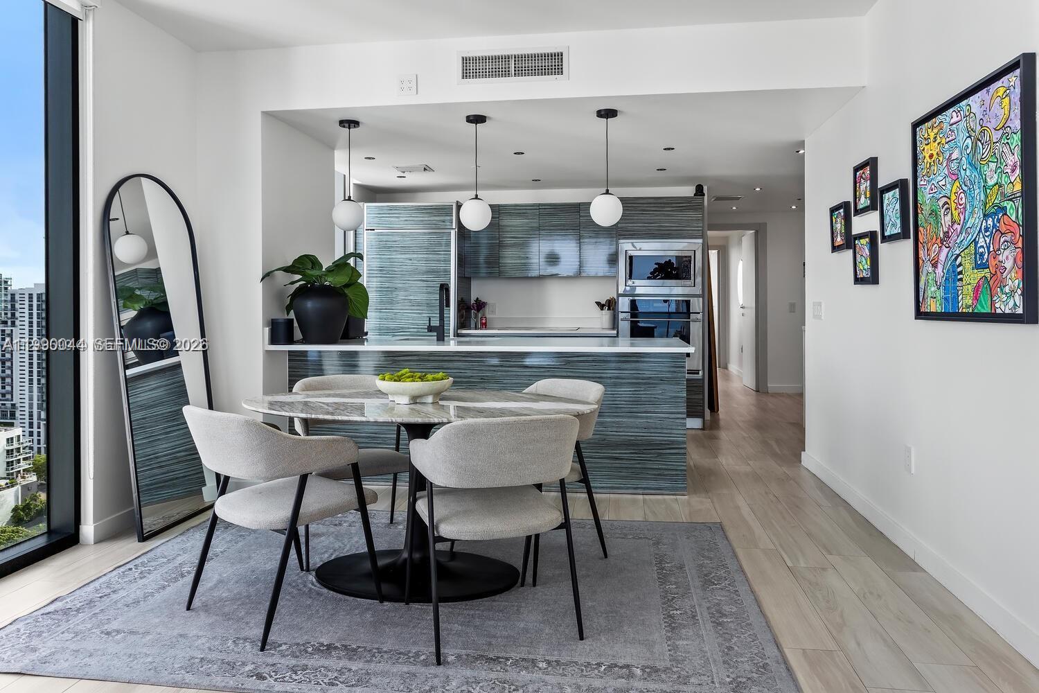 A dining area with a round marble table sits before a modern kitchen with blue-toned cabinetry — 460 NE 28th St # 2008, Miami FL 33137, MIAMI, FL