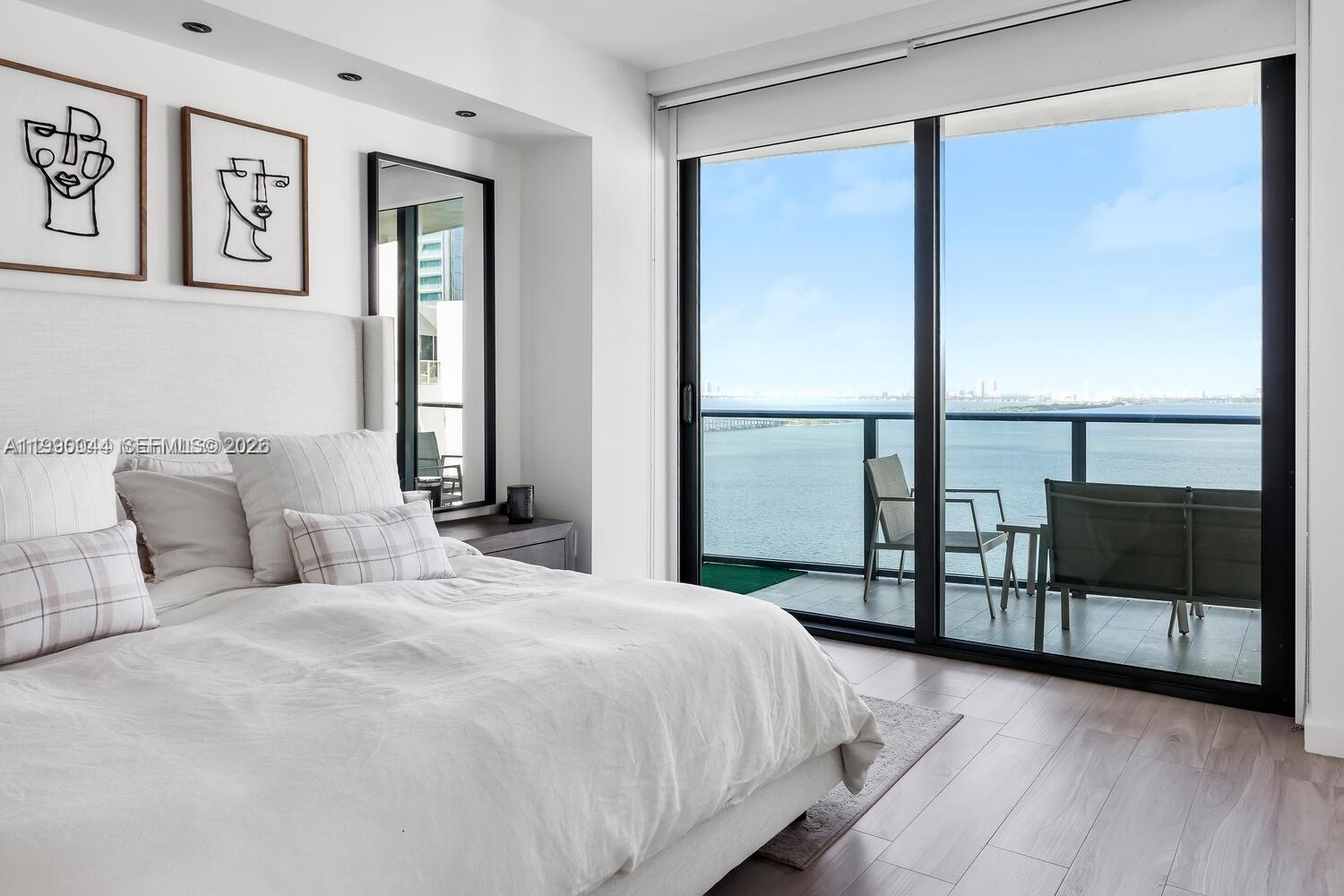 A modern bedroom features a white bed, minimalist line art, and a balcony overlooking water — 460 NE 28th St # 2008, Miami FL 33137, MIAMI, FL
