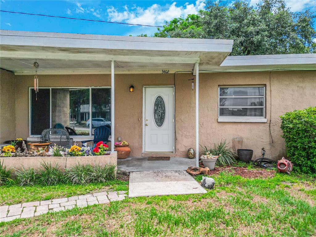 A single-story house exterior features a covered porch, a white front door, and a small garden — 3402 NEEDLES DRIVE, ORLANDO, FL