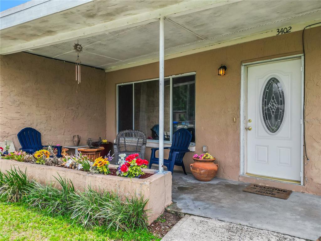 A covered front porch features a concrete floor, a planter box, and outdoor seating — 3402 NEEDLES DRIVE, ORLANDO, FL