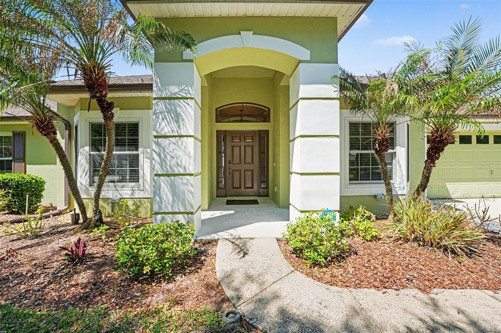 The exterior of a light green house features a covered entryway with white columns — 122 COSTA LOOP, AUBURNDALE, FL