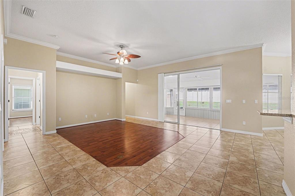 An open living area features a central wood-floored section surrounded by light-colored tile flooring — 122 COSTA LOOP, AUBURNDALE, FL
