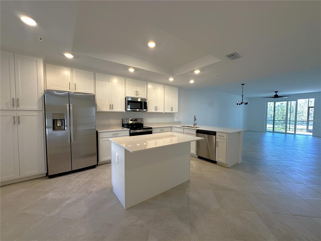 A modern kitchen features white cabinetry, stainless steel appliances, a center island, and tile flooring — 14231 HERITAGE LANDING BOULEVARD UNIT 1918, PUNTA GORDA, FL