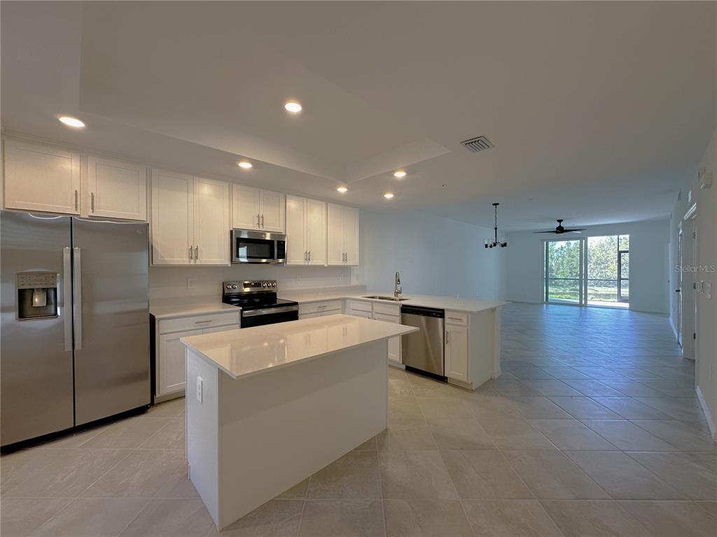 A kitchen with white cabinets, stainless steel appliances, and an island opens to a living area — 14231 HERITAGE LANDING BOULEVARD UNIT 1918, PUNTA GORDA, FL