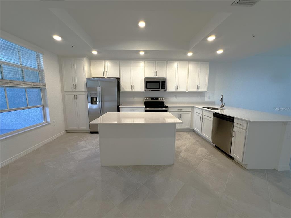 A kitchen features white cabinets, stainless steel appliances, a center island, and light tile flooring — 14231 HERITAGE LANDING BOULEVARD UNIT 1918, PUNTA GORDA, FL