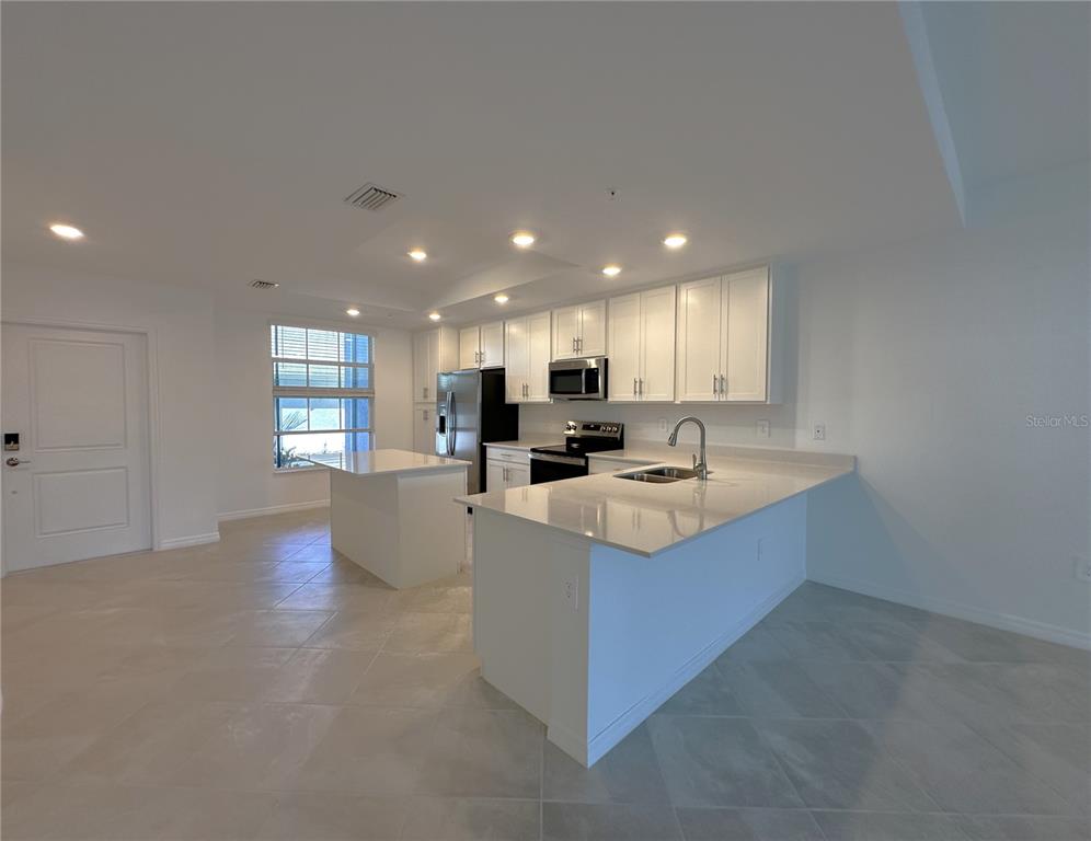 A modern kitchen features white cabinetry, quartz countertops, a center island, and tile flooring — 14231 HERITAGE LANDING BOULEVARD UNIT 1918, PUNTA GORDA, FL