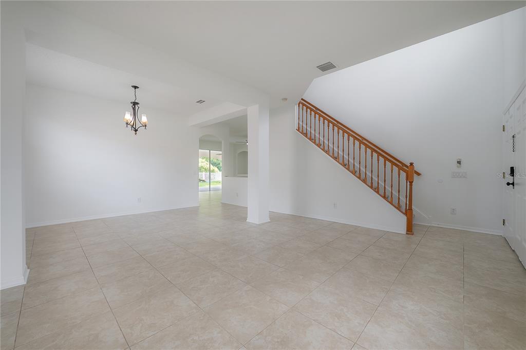 A bright, tiled foyer features a wooden staircase with a railing and a dining area — 4716 MAPLETREE LOOP, WESLEY CHAPEL, FL