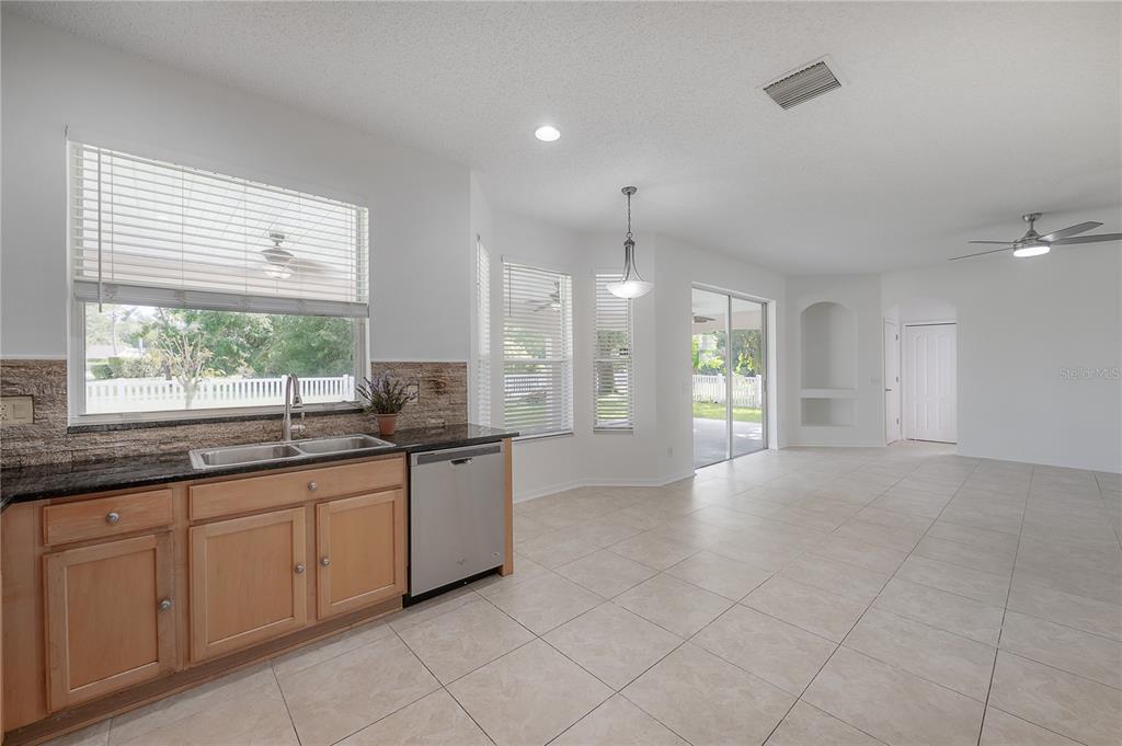 A kitchen with light wood cabinets, dark countertops, and tile flooring opens to a living area — 4716 MAPLETREE LOOP, WESLEY CHAPEL, FL