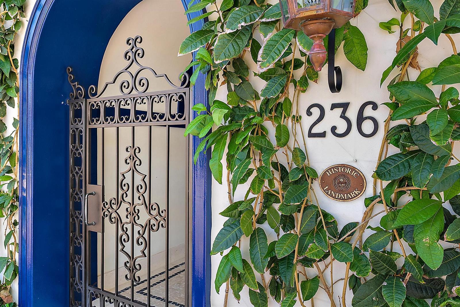 A wrought iron gate stands beside a white wall with a historic landmark plaque — 236 Phipps Plaza # 101, Palm Beach FL 33480, PALM BEACH, FL
