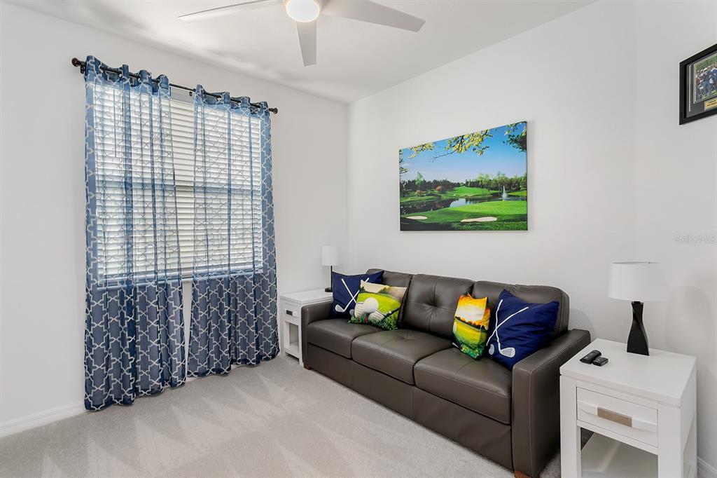 A room features a dark leather sofa, golf-themed decor, white end tables, and blue curtains — 18028 GAWTHROP DRIVE UNIT 108, BRADENTON, FL