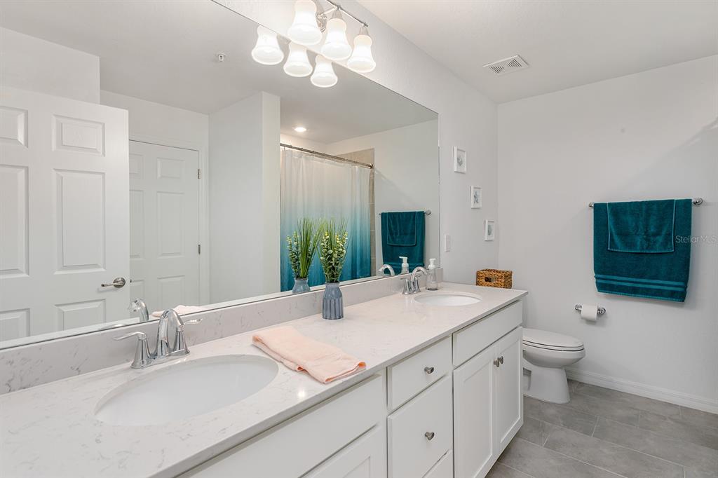 A bathroom features a double vanity with white cabinets, quartz countertops, and a large mirror — 18028 GAWTHROP DRIVE UNIT 108, BRADENTON, FL