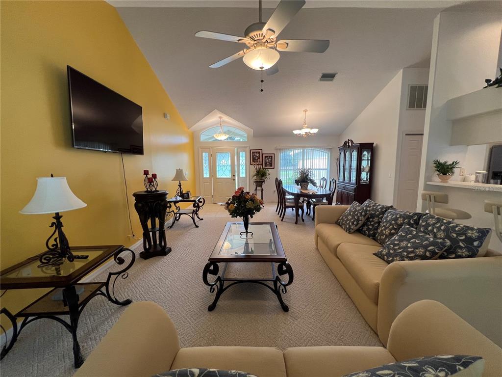 A living room with a yellow wall, vaulted ceiling, beige carpet, and dining area beyond — 9998 N LANGDON ROAD, CITRUS SPRINGS, FL