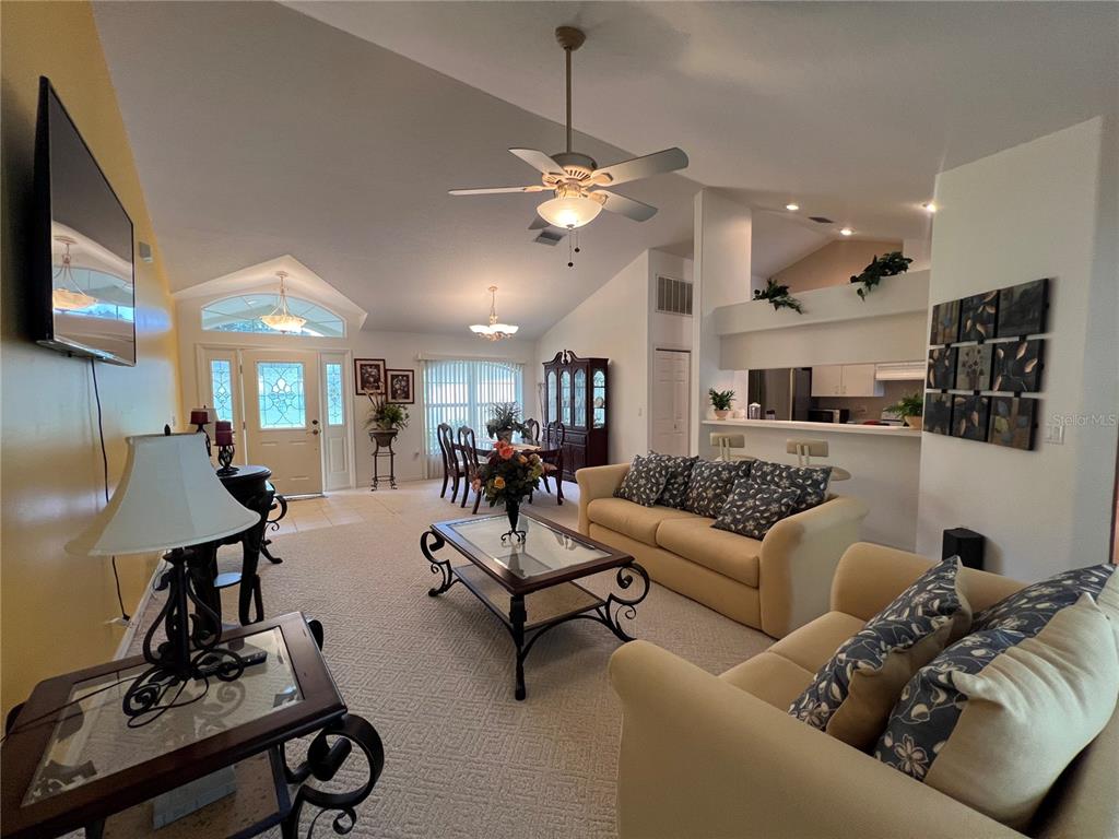 A living room features vaulted ceilings, carpeted floors, a ceiling fan, and an adjacent kitchen — 9998 N LANGDON ROAD, CITRUS SPRINGS, FL