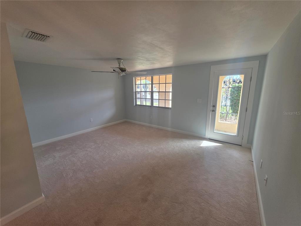 An empty room features light blue walls, beige carpeting, a ceiling fan, and a glass door — 4461 RUSTIC DRIVE, NEW PORT RICHEY, FL