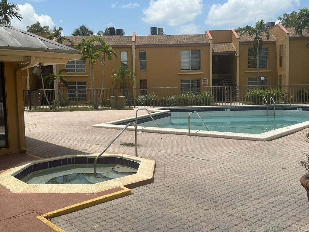 An outdoor pool and hot tub area with a multi-story apartment building in the background — 4545 Treehouse Lane # G, Tamarac FL 33319, TAMARAC, FL