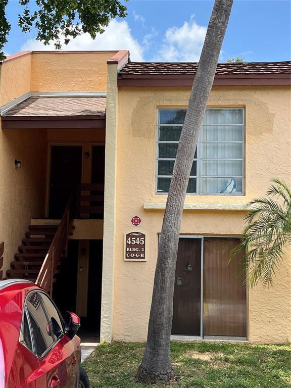 A two-story tan apartment building exterior features a palm tree and a red car — 4545 Treehouse Lane # G, Tamarac FL 33319, TAMARAC, FL
