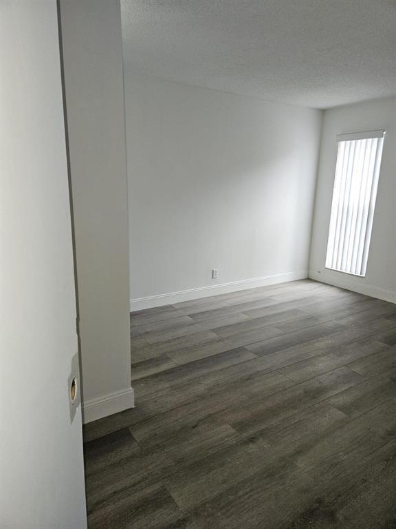 An empty room with gray wood-look flooring, white walls, and a vertical blind window — 4545 Treehouse Lane # G, Tamarac FL 33319, TAMARAC, FL