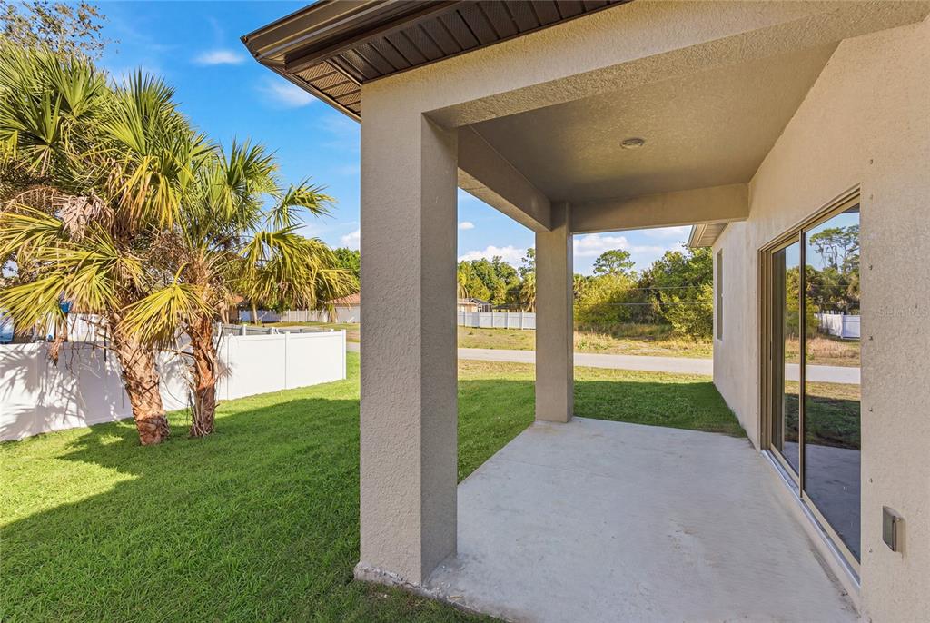 A covered concrete patio overlooks a grassy backyard with palm trees and a white fence — 3783 CORDOVA TERRACE, NORTH PORT, FL