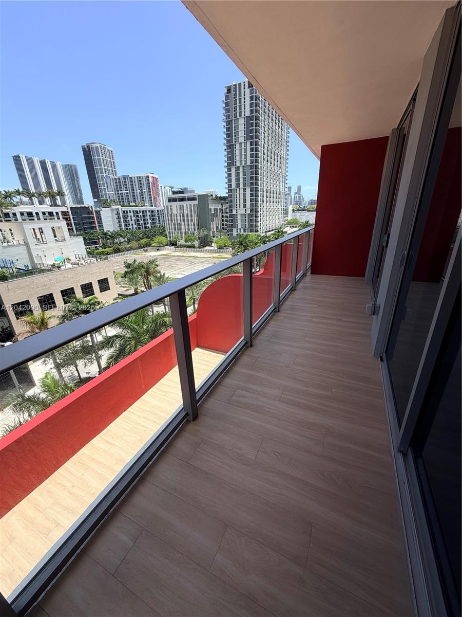 A balcony with wood-look flooring, glass railings, and red accent walls overlooks a city skyline — 90 NE 32nd St # 706, Miami FL 33137, MIAMI, FL