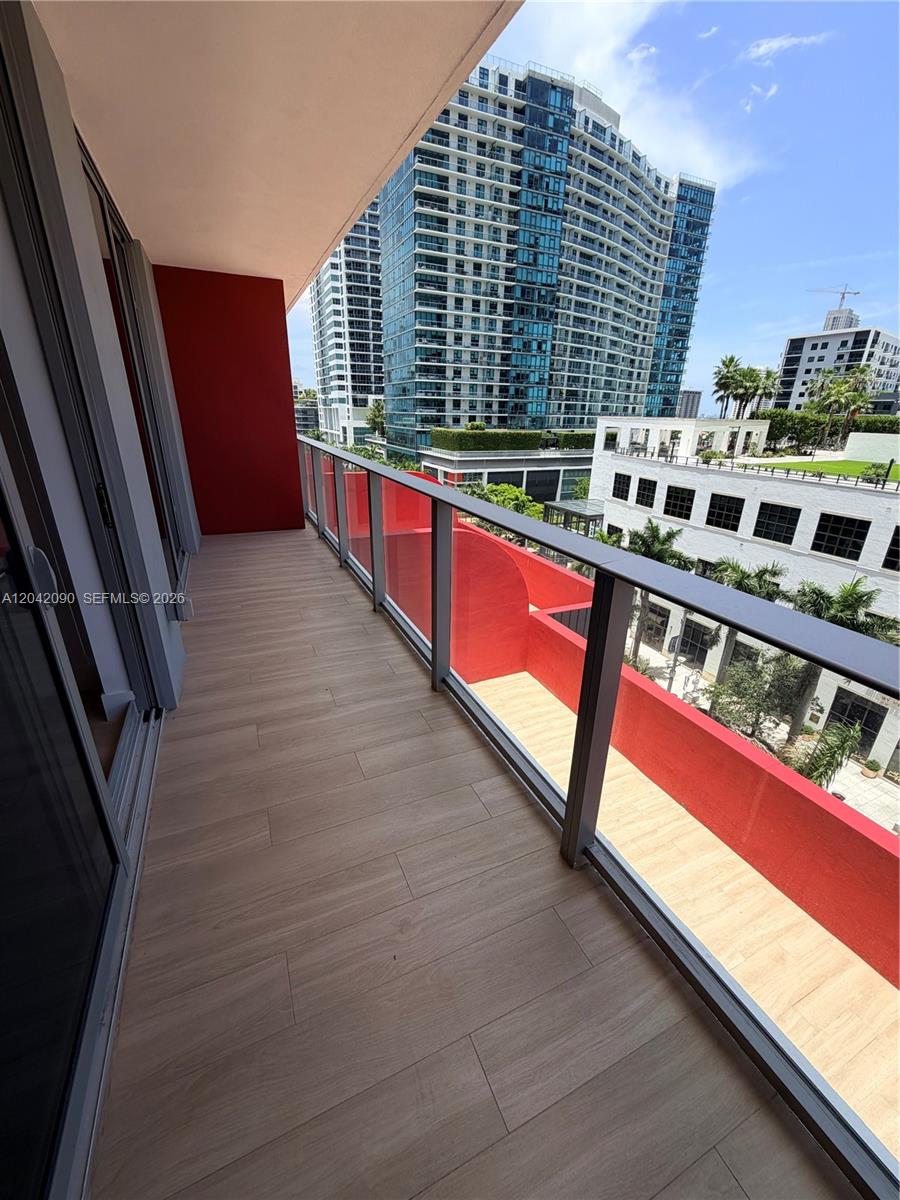 A balcony with wood-look tile flooring, a glass railing, and red accent walls — 90 NE 32nd St # 706, Miami FL 33137, MIAMI, FL