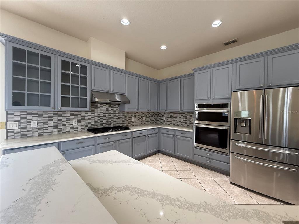 A kitchen features blue cabinets, stainless steel appliances, a tiled backsplash, and a quartz island — 4495 HARTS COVE WAY, CLERMONT, FL