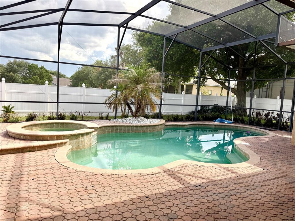A screened-in patio features a swimming pool, an attached hot tub, and paver decking — 4495 HARTS COVE WAY, CLERMONT, FL