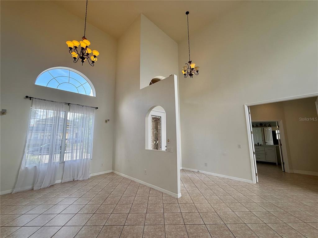 A high-ceilinged room with tile flooring, two chandeliers, and a central partition wall — 4495 HARTS COVE WAY, CLERMONT, FL