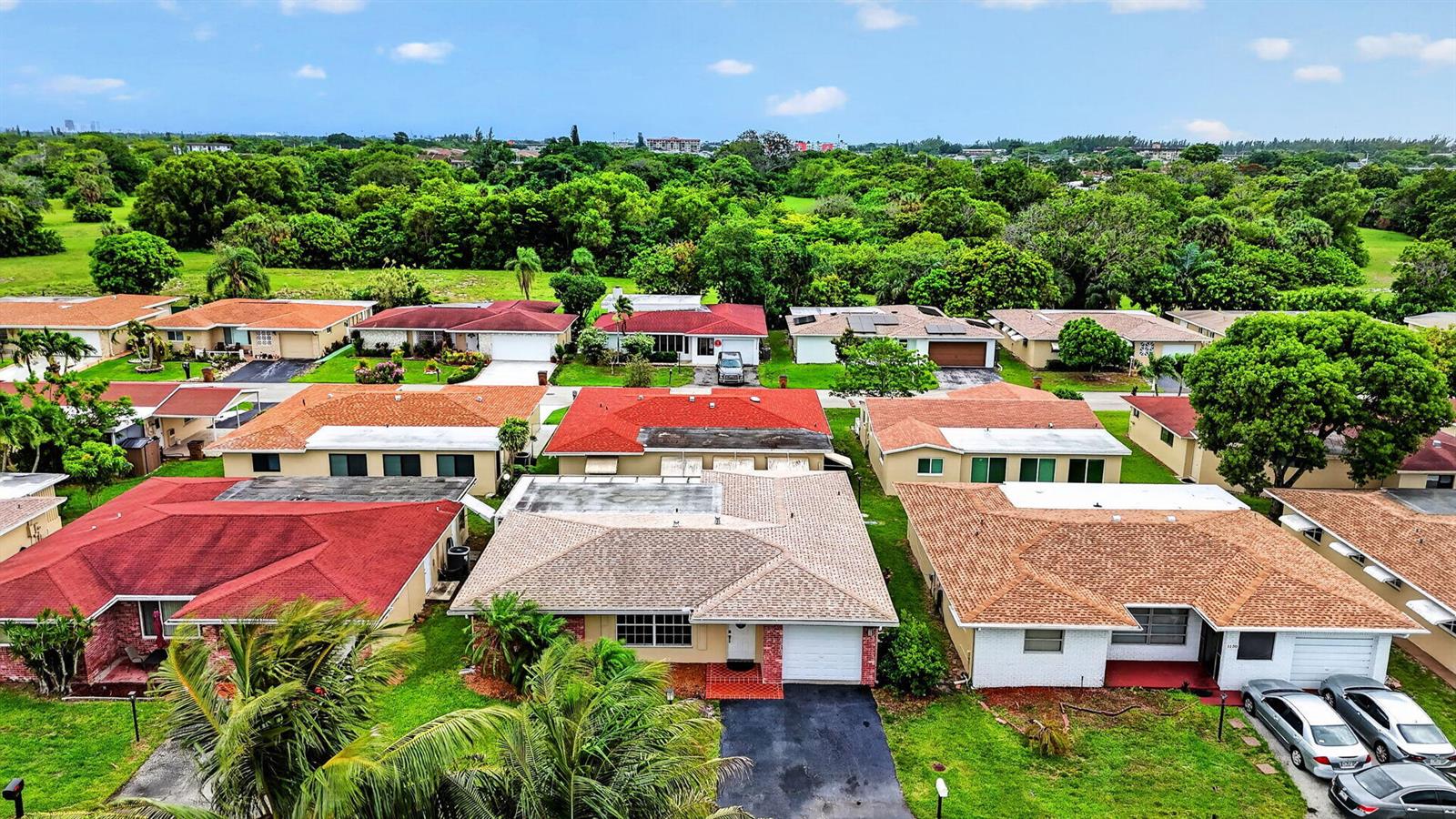 An aerial view shows a suburban neighborhood with several single-story houses and lush green trees — 1140 NW 49th Street, Deerfield Beach FL 33064, DEERFIELD BEACH, FL