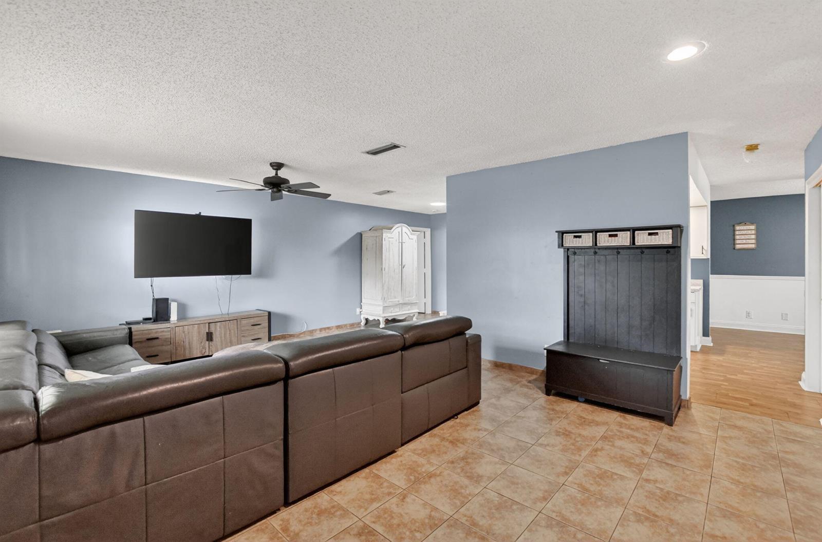 A living room features a large sectional sofa, a wall-mounted television, and tile flooring — 1140 NW 49th Street, Deerfield Beach FL 33064, DEERFIELD BEACH, FL