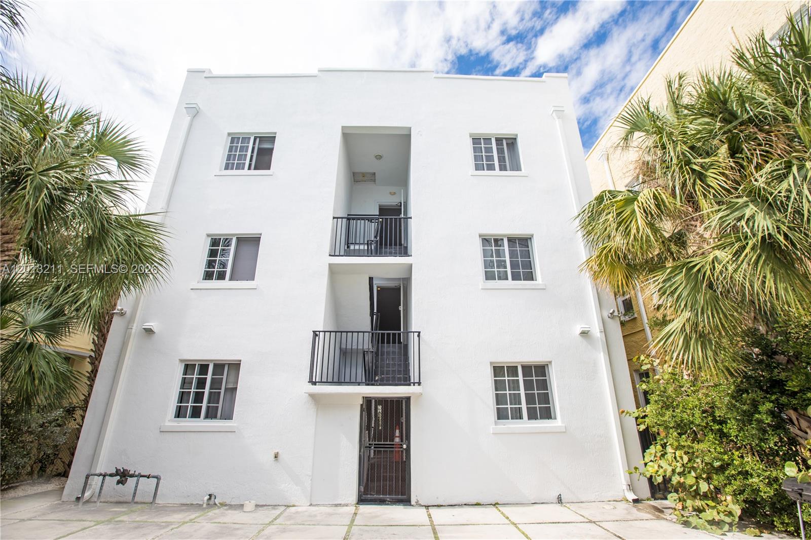 A three-story white stucco apartment building features exterior balconies and a ground-level metal security door — 1345 Pennsylvania Ave, Miami Beach FL 33139, MIAMI BEACH, FL