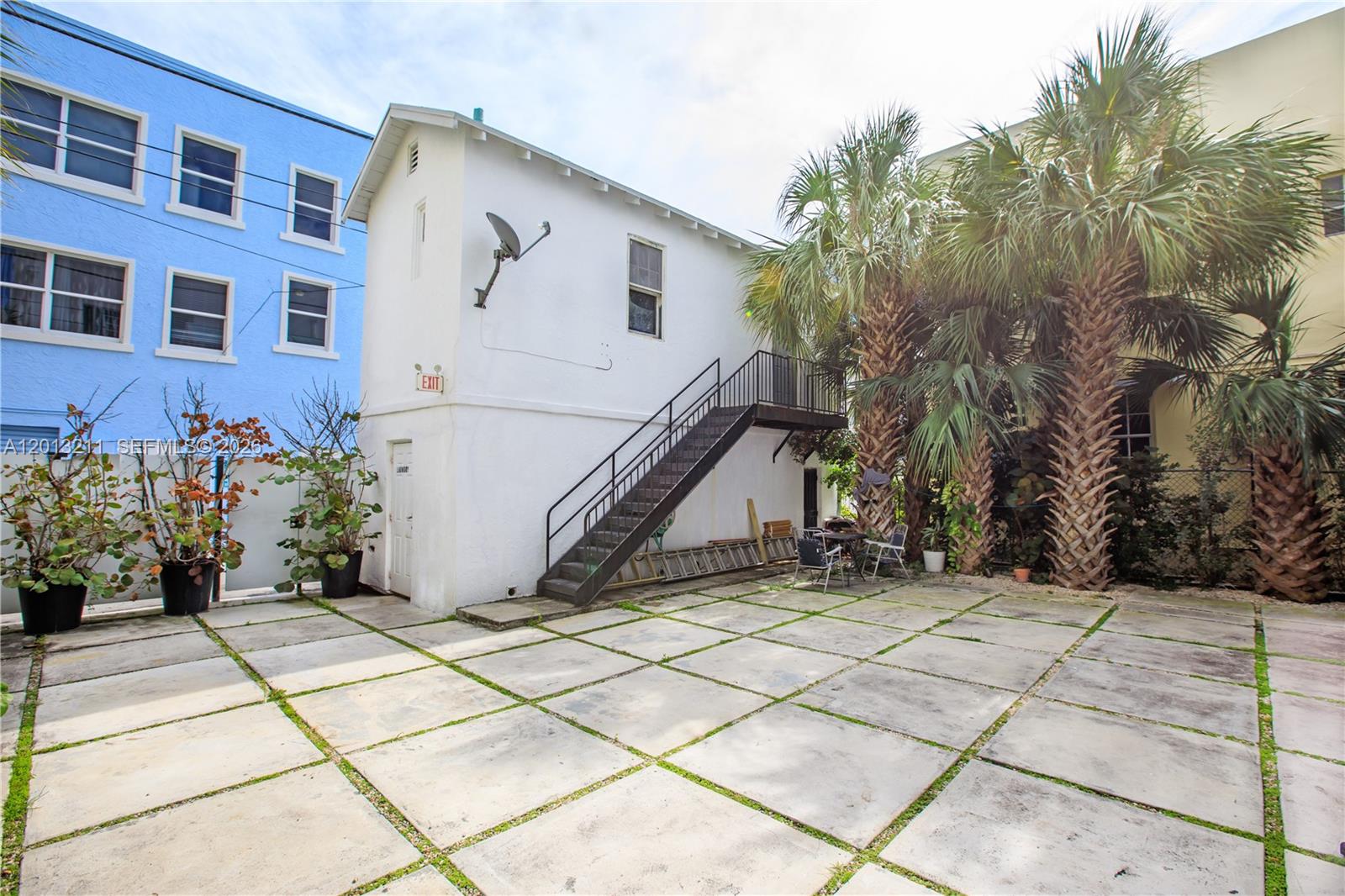 A white two-story building features an exterior staircase and a paved patio with palm trees — 1345 Pennsylvania Ave, Miami Beach FL 33139, MIAMI BEACH, FL