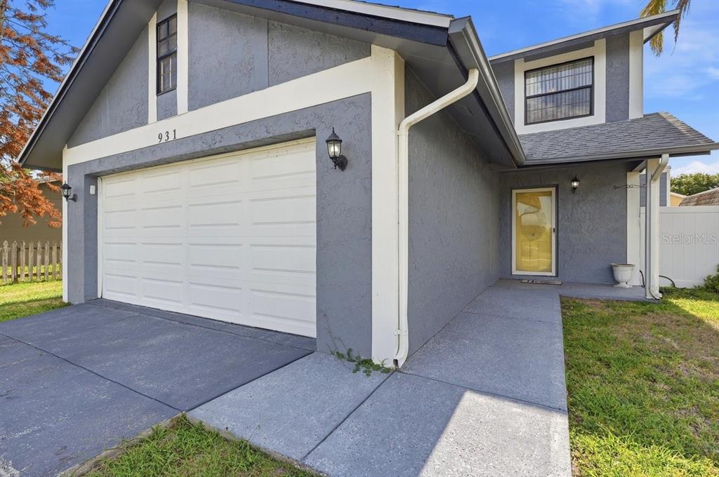 A gray two-story house features a white garage door, a yellow front door, and walkways — 931 WHISPER LAKE DRIVE, WINTER HAVEN, FL