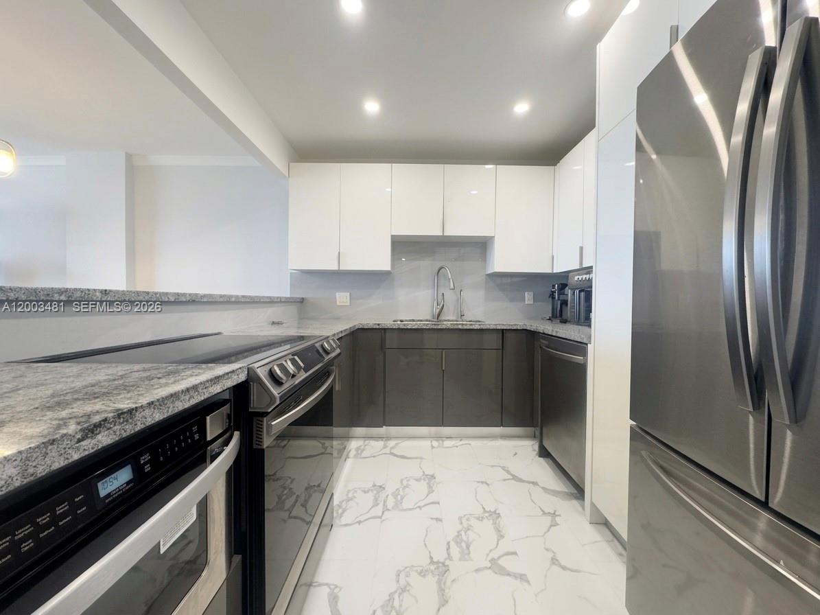A modern kitchen features white upper cabinets, gray lower cabinets, granite countertops, and marble-patterned flooring — 3800 S Ocean Dr # 802, Hollywood FL 33019, HOLLYWOOD, FL