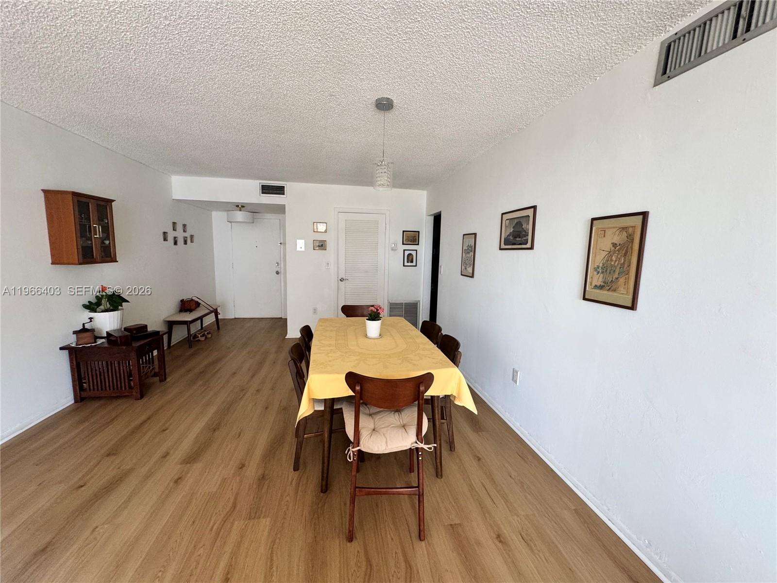 A dining room features wood-look flooring, a yellow tablecloth, and several framed wall pictures — 1470 NE 125th Ter # 407, North Miami FL 33161, NORTH MIAMI, FL