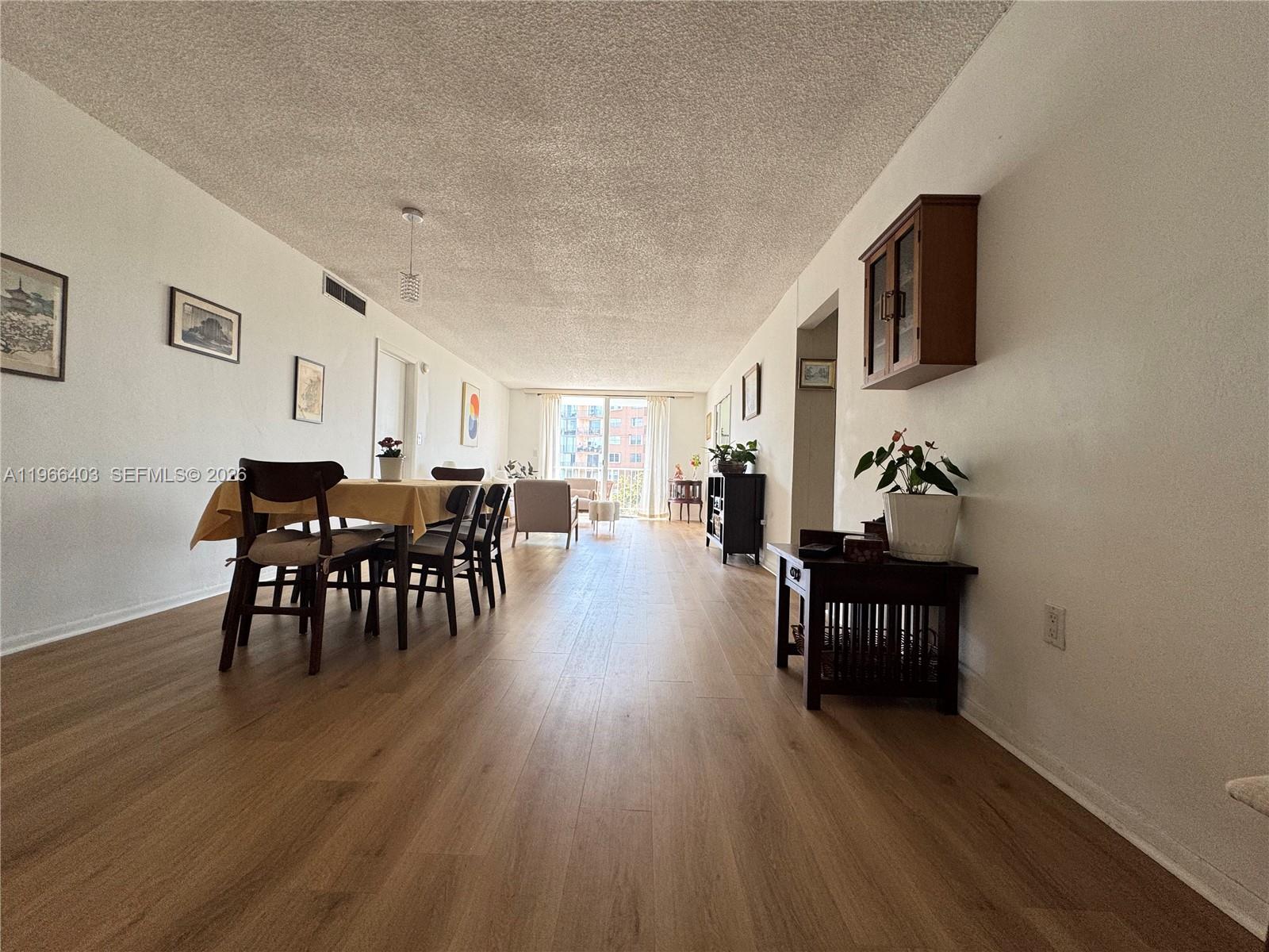 A dining and living area features wood-look flooring, a popcorn ceiling, and a balcony view — 1470 NE 125th Ter # 407, North Miami FL 33161, NORTH MIAMI, FL