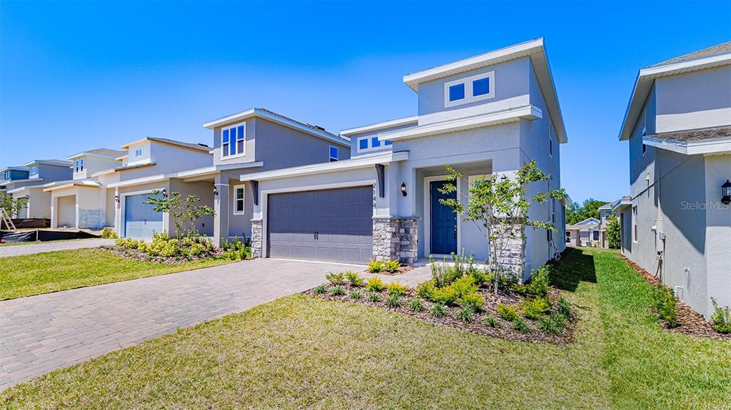 A two-story suburban house with a gray exterior, stone accents, and a paved driveway — 2144 SUNSHINE PEAK DRIVE, MINNEOLA, FL