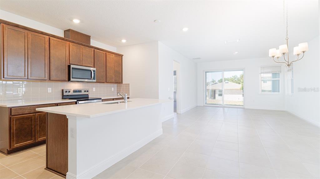 A kitchen with dark wood cabinets, white countertops, and an island opens to a dining area — 2144 SUNSHINE PEAK DRIVE, MINNEOLA, FL