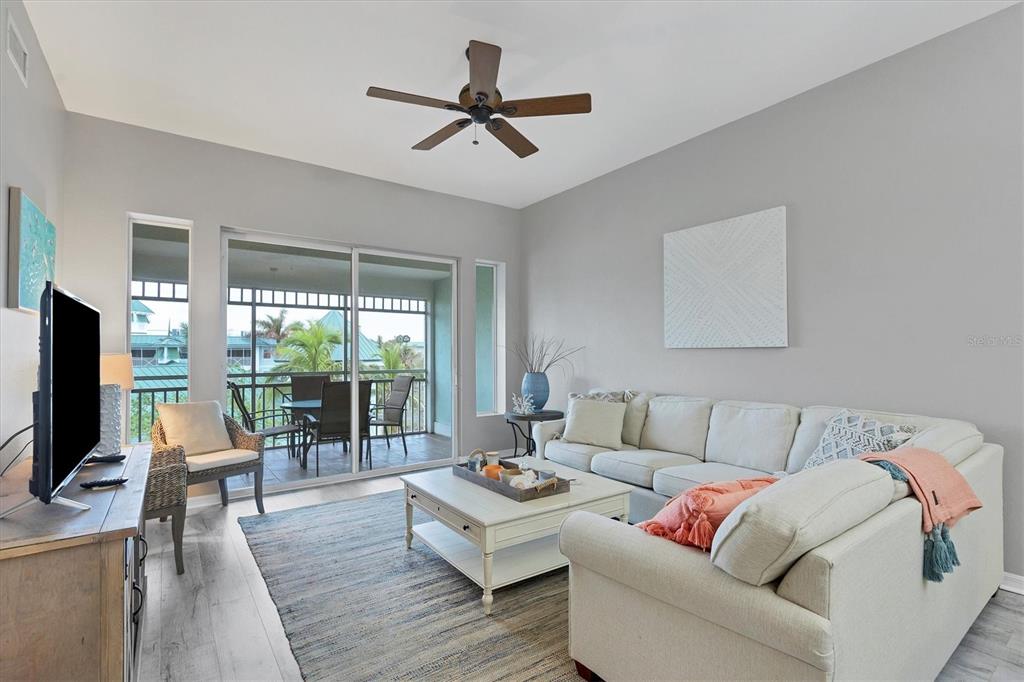 A living room features a sectional sofa, a coffee table, and a balcony with outdoor seating — 5117 MELBOURNE STREET UNIT B4302, PORT CHARLOTTE, FL